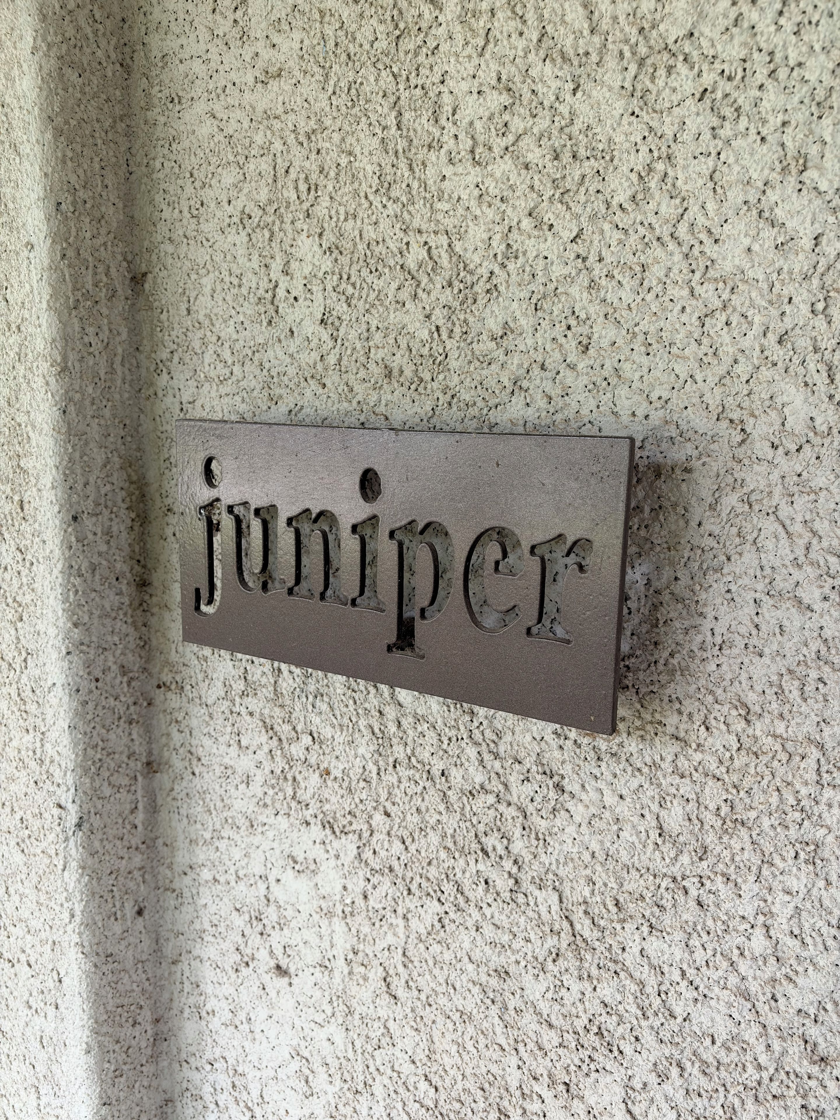 Una pared texturizada con un letrero rectangular que dice 'juniper'.