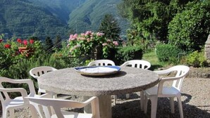 Ein runder Steintisch mit weißen Plastikstühlen in einem Garten, im Hintergrund Berge.