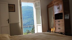 Ein Schlafzimmer mit einem Bett, einer Holzkommode und Blick auf einen Berg und einen See.