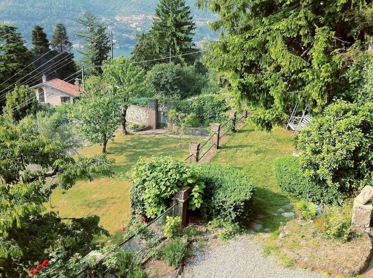 A rural landscape with a stone house, lush greenery, and a clear view of a valley in the background.