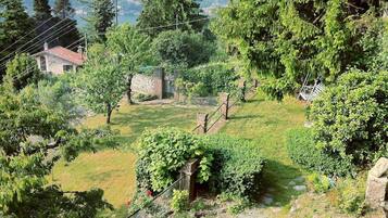 A rural landscape with a stone house, lush greenery, and a clear view of a valley in the background.