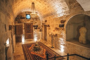 A stone-walled corridor with a chandelier, wooden doors, and a patterned rug.