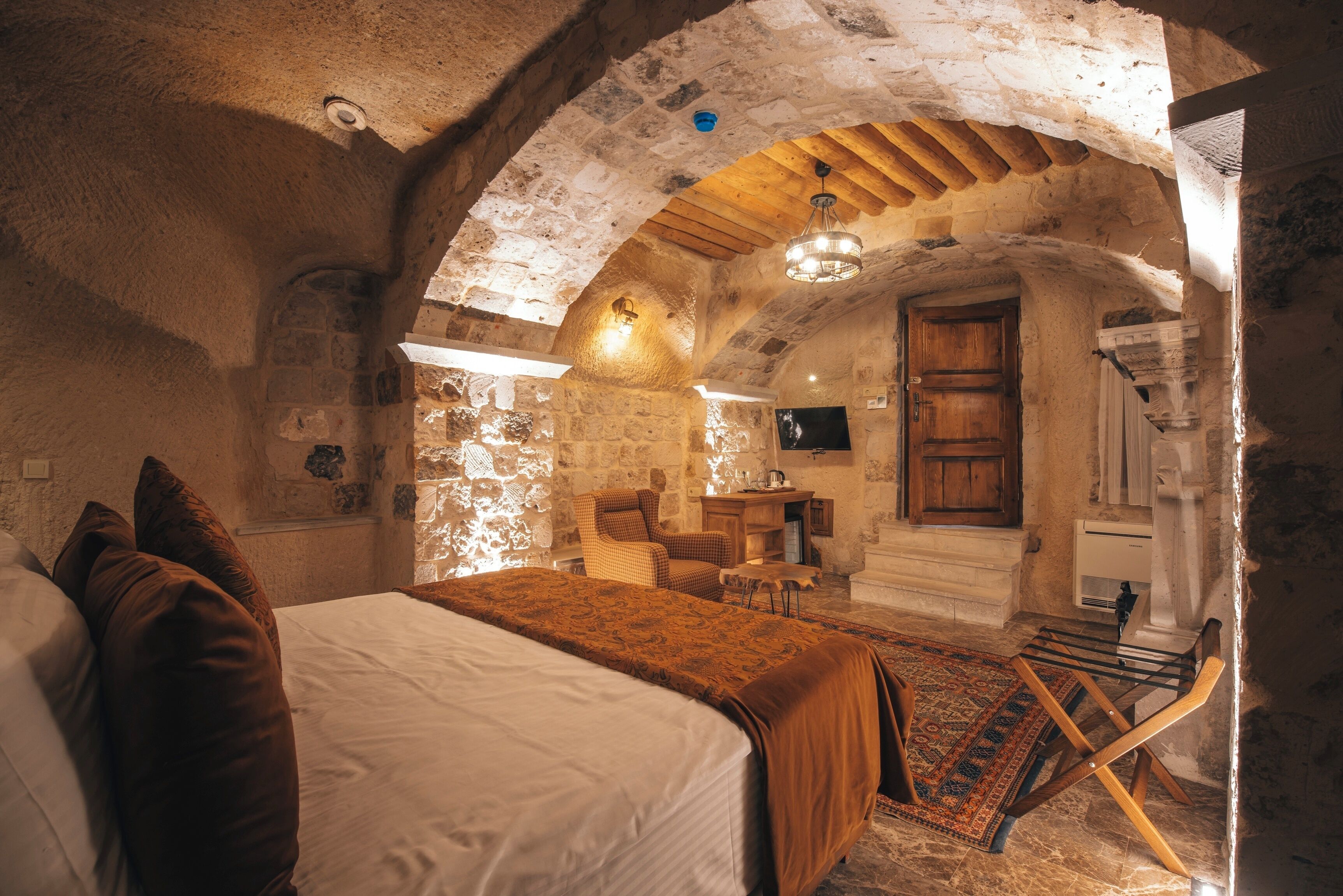 A rustic room with a bed, a wooden chair, a small table, and a stone wall.