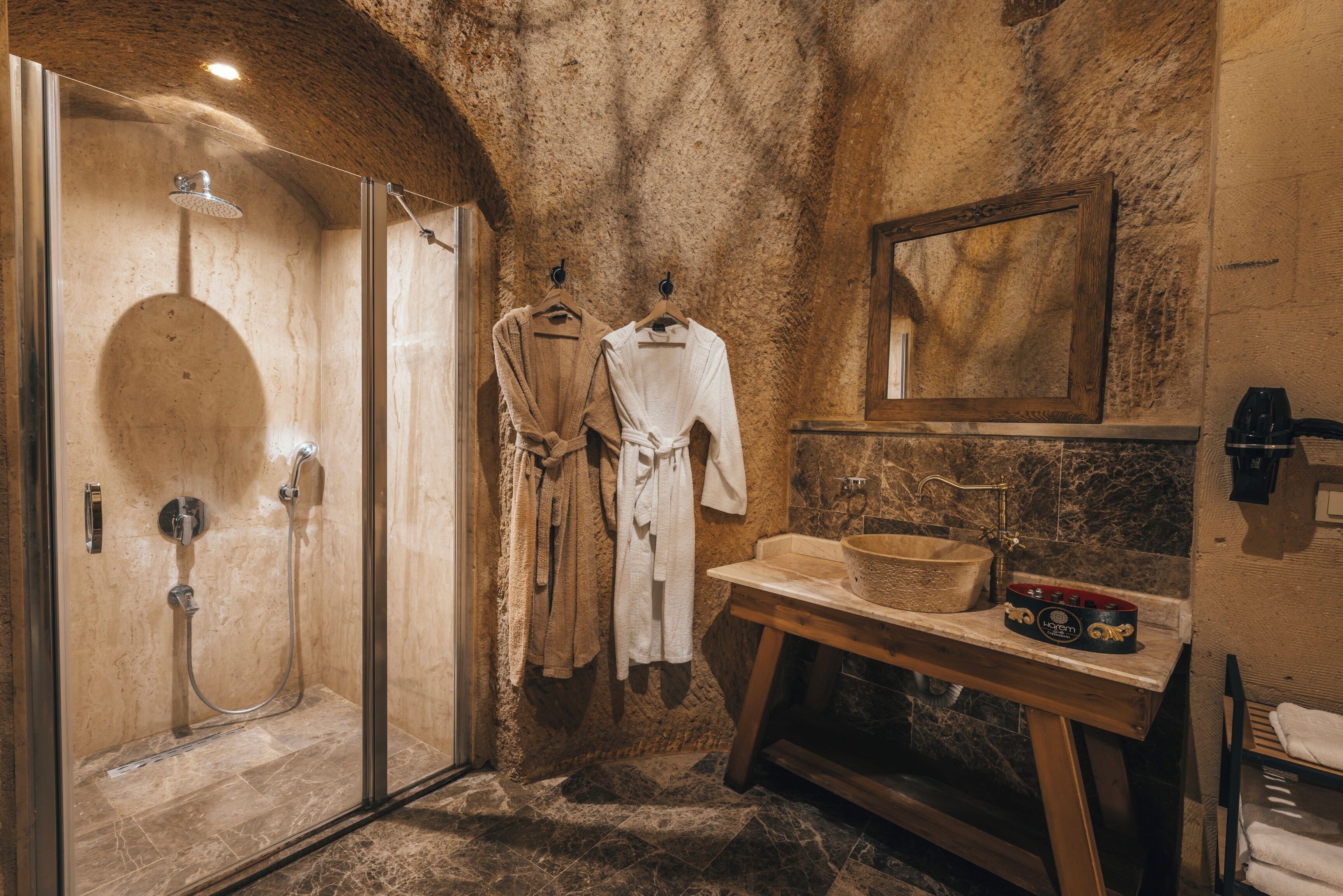 Un baño rústico con ducha envuelta en vidrio, tocador de madera y paredes de piedra.