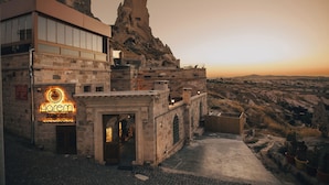 Um hotel com fachada de pedra, uma grande formação rochosa ao fundo e uma placa com a inscrição 'Harem Suites'.