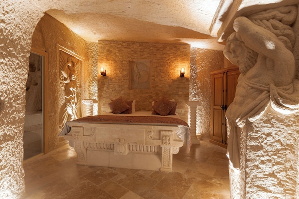 A stone-walled bedroom with a bed, two wall-mounted lights, and a wooden door. - Harem Suites Cappadocia (Nevsehir)