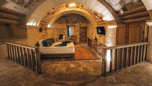 Um quarto com soalho de pedra, cama com almofadas, balaústres de madeira e um arco de pedra.