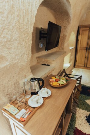 A cozy dining area with a wooden table set for two, a bowl of fruit, a coffee pot, and a television mounted on the wall.