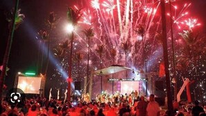 Een concert met een podium en publiek, omgeven door palmbomen.
