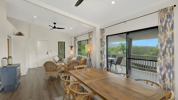 A spacious room with a wooden dining table and chairs, a ceiling fan, and a balcony with a view of greenery. - Hibiscus Hideaway Valla Beach 4BR home w/ two verandahs (Valla Beach)