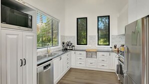 A modern kitchen with white cabinets, stainless steel appliances, and a window with blinds. - Hibiscus Hideaway Valla Beach 4BR home w/ two verandahs (Valla Beach)
