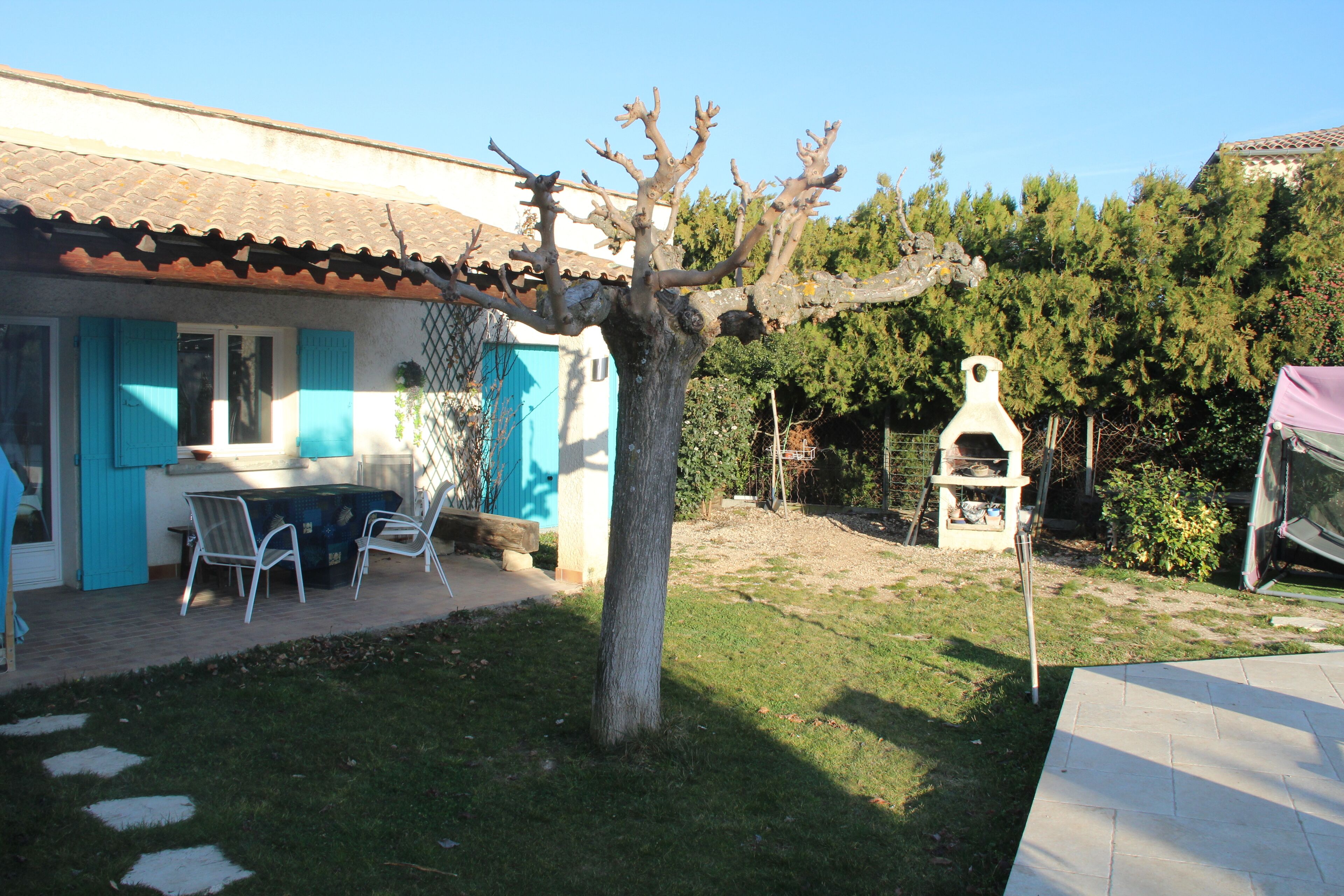 A patio with a table and chairs, a tree, and a building with blue shutters.