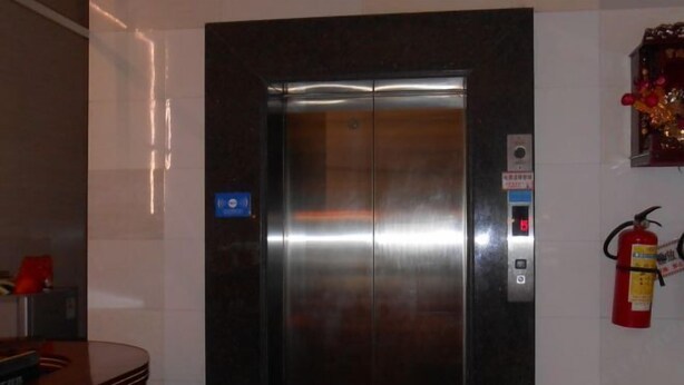 An elevator with a control panel, a fire extinguisher, and a small blue sign on the wall. - Yuxing Hostel (Jieyang)