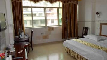 A hotel room with a bed, a desk, a chair, a television, and a window with curtains.