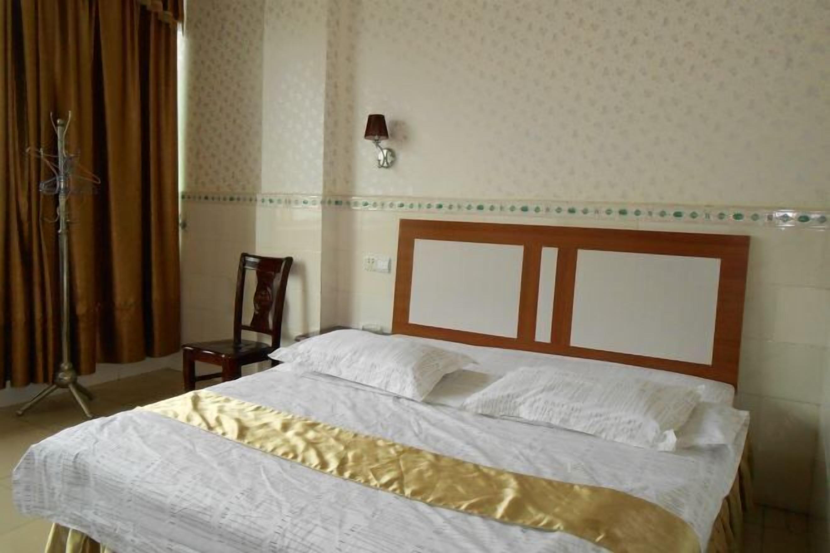 A neatly made bed with a wooden headboard, a chair, and a coat rack in a room with patterned wallpaper and a decorative border.