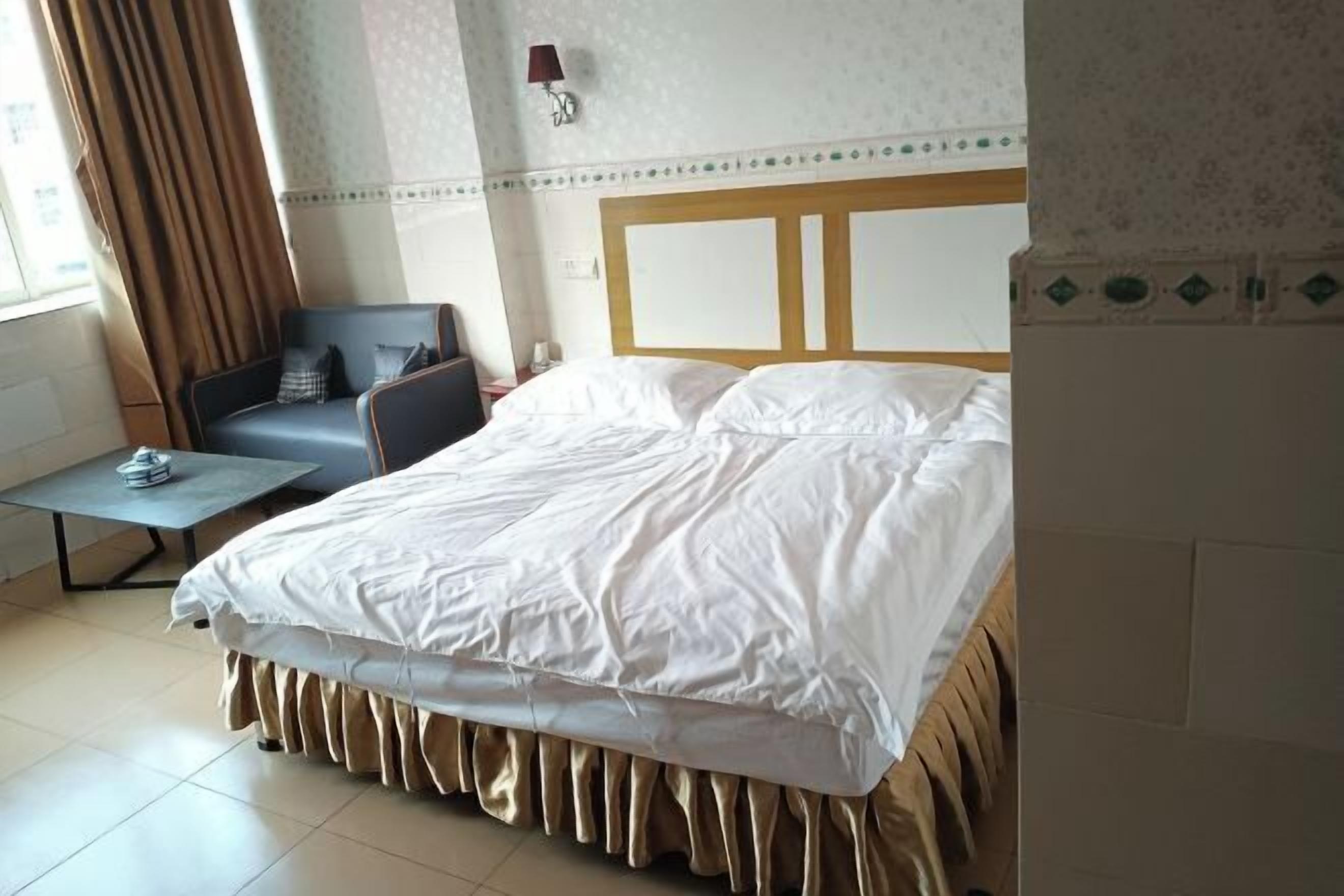 A hotel room with a bed, a chair, a small table, and a lamp.
