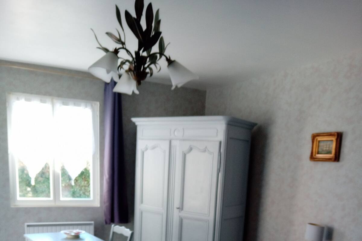 A bedroom with a bed, a white wardrobe, a desk with a chair, and a window with curtains.
