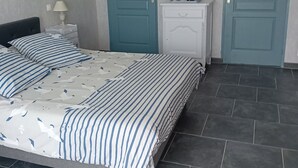 Un dormitorio con cama, dos puertas, una mesita de noche, una lámpara y una pequeña mesa con tetera y tazas.