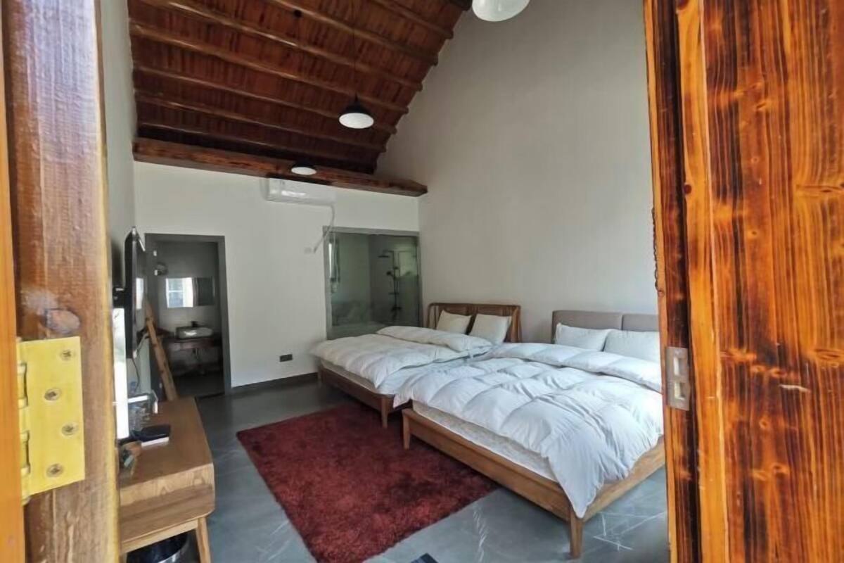 Une chambre avec un plafond en bois, un lit avec une literie blanche, un tapis rouge et une table de chevet en bois.