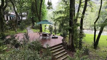 A patio with a table and chairs, surrounded by trees and a brick pathway.