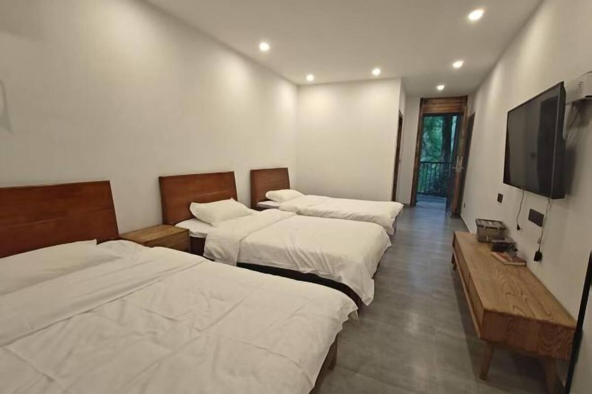 Une chambre d’hôtel avec trois lits, un banc en bois, une télévision et une porte donnant sur un balcon.