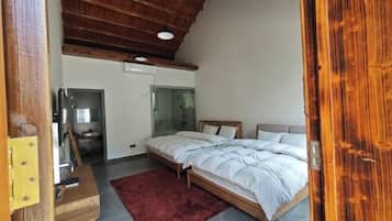 A bedroom with a wooden ceiling, a bed with white bedding, a red rug, and a small wooden table.