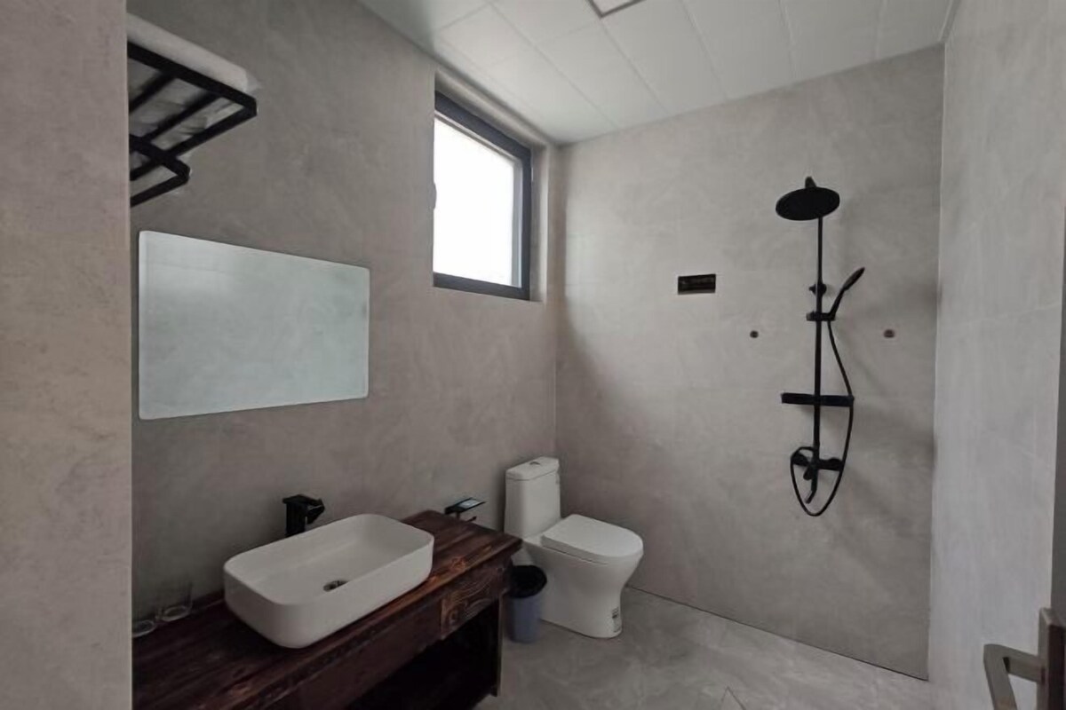 A modern bathroom with a large mirror, a white sink, a toilet, and a shower.