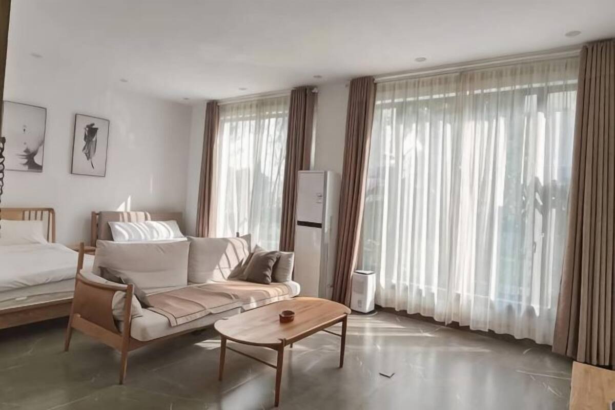 Une chambre d’hôtel moderne équipée d’un lit, d’un canapé, d’une table basse et de grandes fenêtres avec des rideaux.