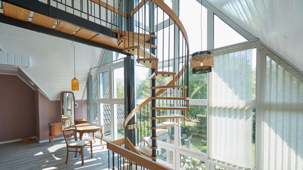 Una habitación amplia con una escalera espiral de madera, ventanas grandes y vistas al exterior.