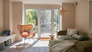 Una sala de estar moderna con un sofá verde, una silla de mimbre y un amplio ventanal corredera que da a un balcón.