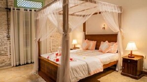 A four-poster canopy bed with a wooden headboard, two bedside tables with lamps, and a stone wall. - Ceylon Kingsmen Garden Hotel (Negombo)