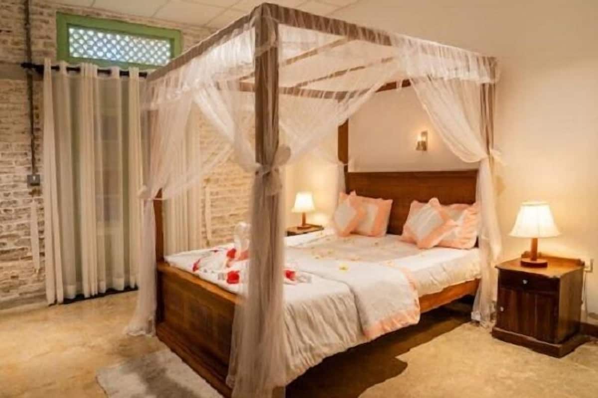 A four-poster canopy bed with a wooden headboard, two bedside tables with lamps, and a stone wall.