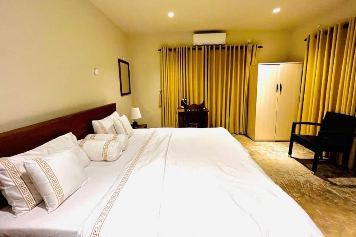 A hotel room with a large bed, a desk with a chair, a wardrobe, and curtains.
