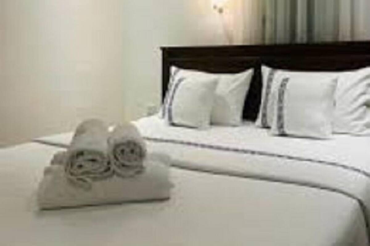 A hotel room with a neatly made bed, a wall-mounted light, and a window with curtains.