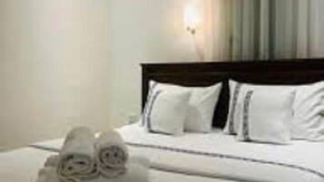 Una habitación de hotel con una cama bien hecha, una lámpara de pared y un ventanal con cortinas.