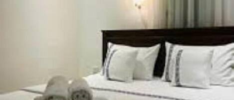 Una habitación de hotel con una cama bien hecha, una lámpara de pared y un ventanal con cortinas.