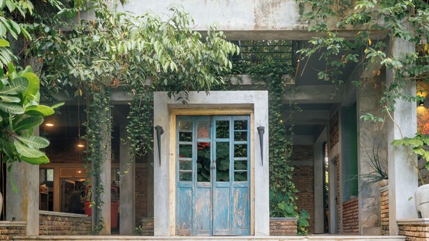 A building entrance with a blue door, steps leading up to it, and surrounding greenery. - Ceylon Kingsmen Garden Hotel (Negombo)