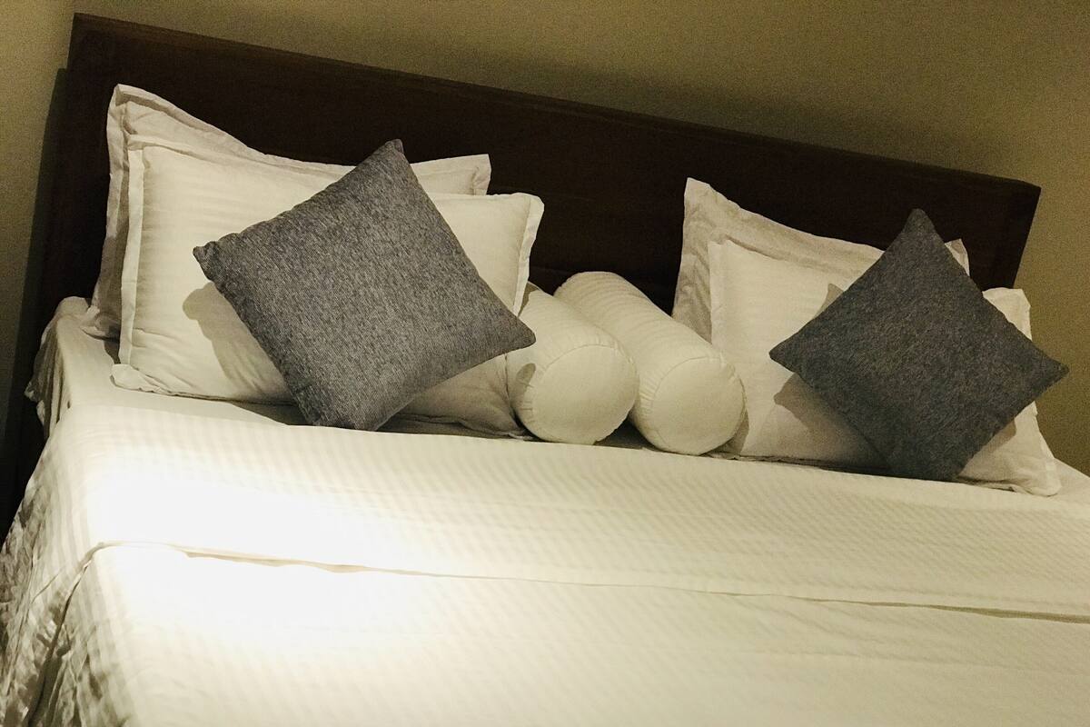 A neatly made bed with white bedding and two dark gray pillows.