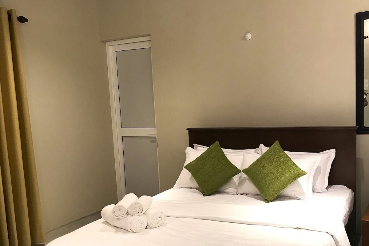 A neatly made bed with white linens and two green pillows, a wooden headboard, and a door with a window to the left.