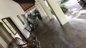 Un espacio al aire libre cubierto con piso de concreto, sillas de madera, una silla colgante y un vehículo estacionado fuera.