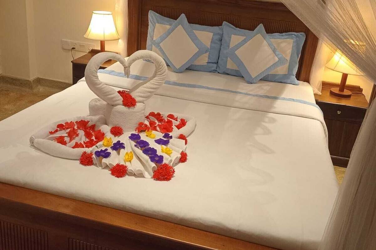 A neatly made bed with a white and blue headboard, a decorative swan, and colorful flowers on the bedspread.