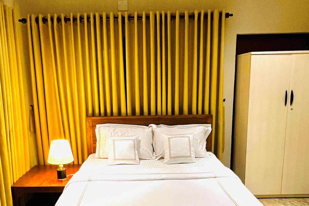 A hotel room with a large bed, a nightstand with a lamp, and a wardrobe.