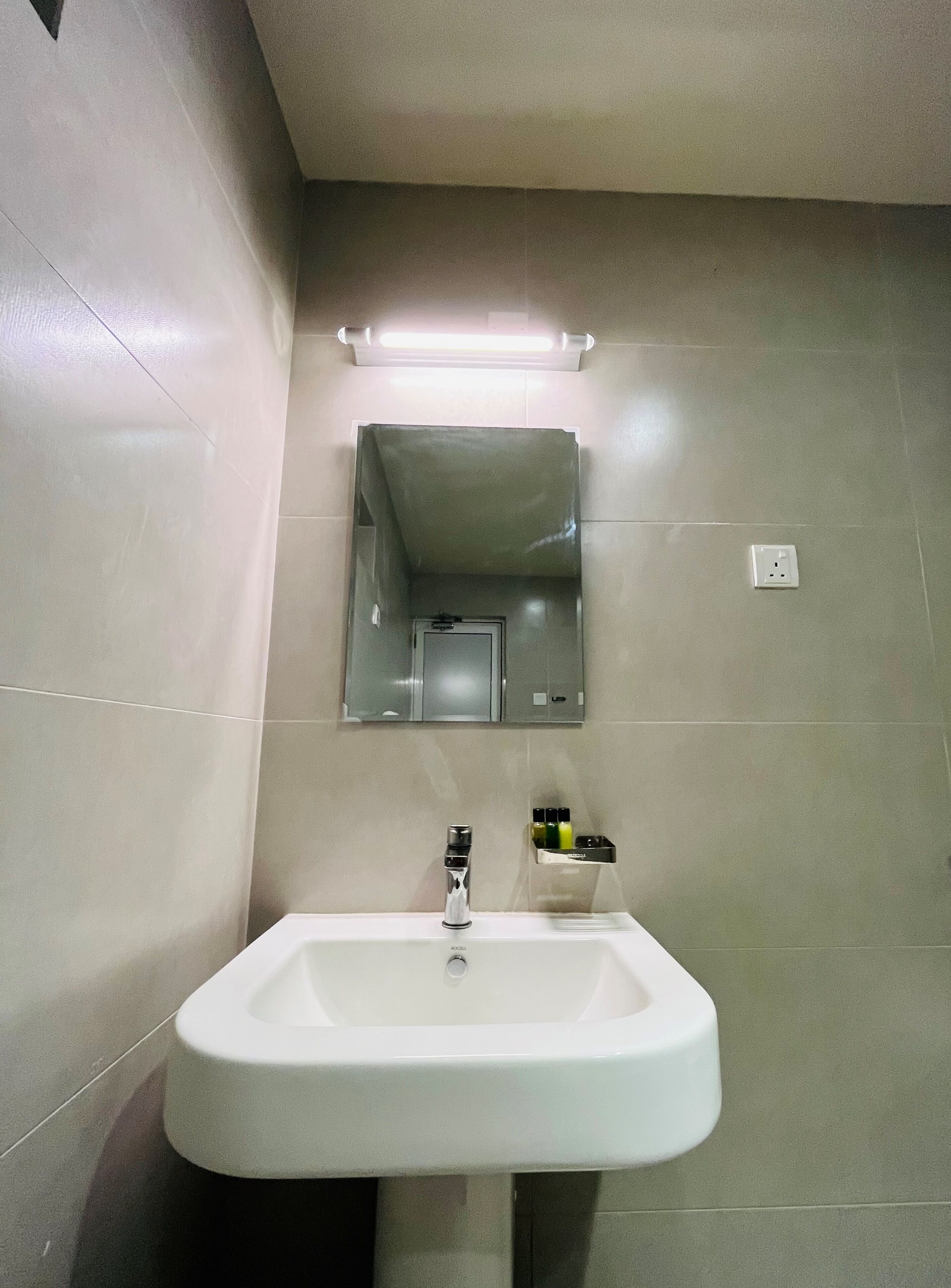 Een badkamer met een wit wastafel, een spiegel en een plank met toiletartikelen.