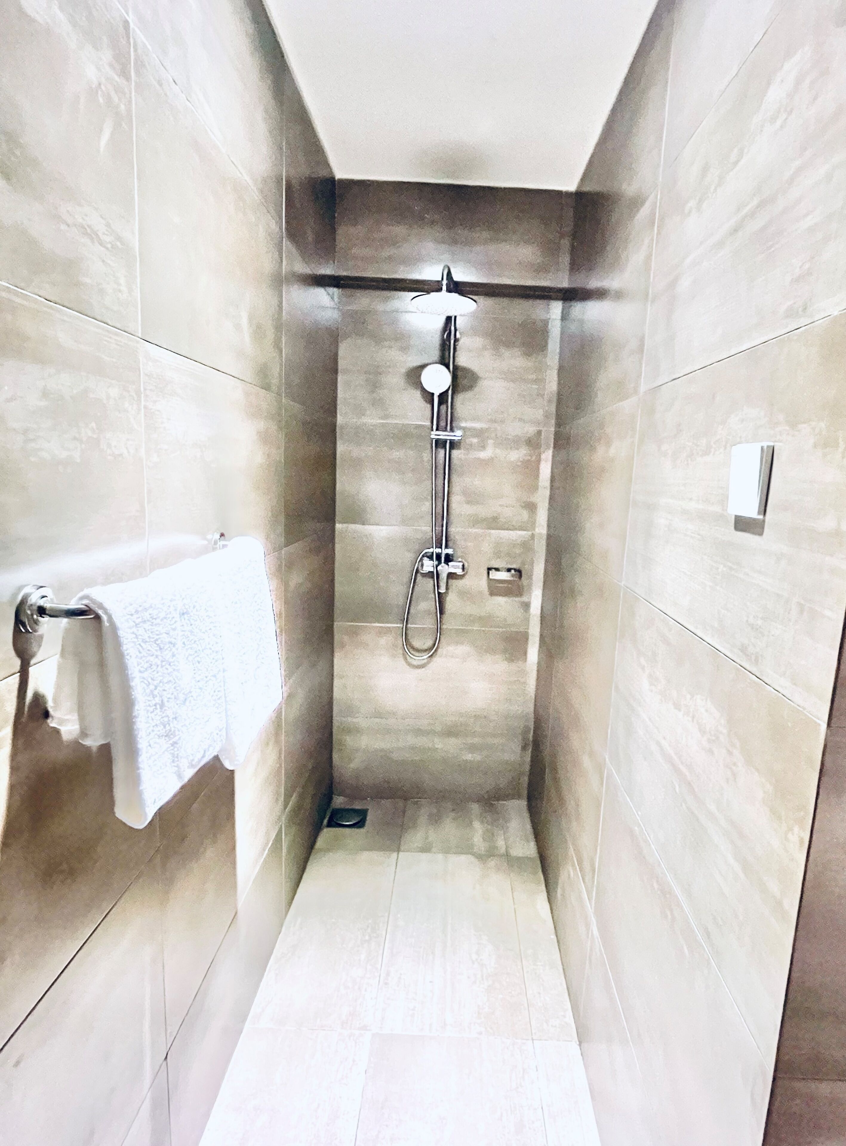 A narrow, tiled shower stall with a handheld showerhead and a wall-mounted control panel.