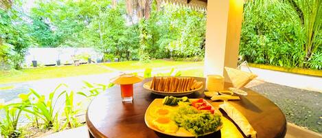 A table with food and drinks, surrounded by lush greenery and a covered area with a wooden ceiling.