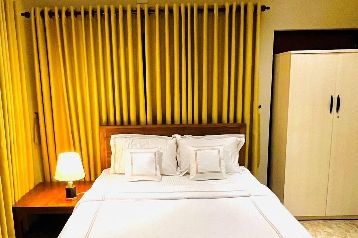 A hotel room with a large bed, a nightstand with a lamp, and a wardrobe.