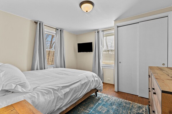 A bedroom with a bed, a flat-screen TV mounted on the wall, and a wardrobe. - Cozy Cape in Smithfield (Smithfield)
