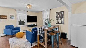 Un salon moderne avec un téléviseur, des fauteuils bleus, une table en bois et un panneau portant l'inscription « Aimez de tout votre cœur ».