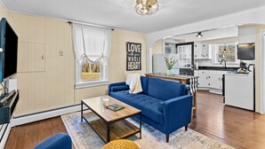 Un salon moderne avec un canapé bleu, une table basse en bois et une cuisine en arrière-plan.