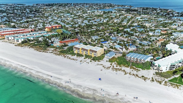 Luftaufnahme einer Küstenstadt mit Strandhäusern, einem Yachthafen und einem großen Hotelkomplex mit mehreren Gebäuden.